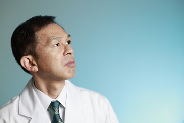 Middle-aged Asian doctor in a white coat on blue background. Concept image of regenerative medicine, vaccine development and advanced therapy.
