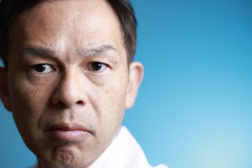Middle-aged Asian doctor in a white coat on blue background. Concept image of regenerative medicine, vaccine development and advanced therapy.