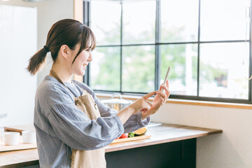 家のキッチン・ダイニングでスマホのアプリを使うアジア人女性
