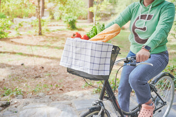 Fototapeta na wymiar Unrecognizable young woman rides her European bike carrying fresh food in the basket. Healthy vegan lifestyle concept.