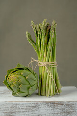A bunch of fresh asparagus and artichoke on a white box made of wood
