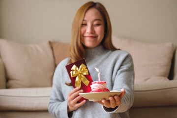 Portrait image of a young woman holding a gift box and birthday cake with candle