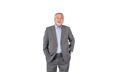 A cheerful elderly man with gray hair and a beard, wearing a gray suit and blue shirt, standing with his hands in his pockets against a white background.
