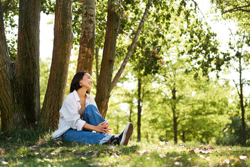 Portrait of asian girl relaxing, leaning on tree and resting in park under shade, smiling and...