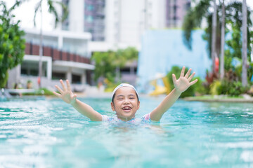 Naklejka premium Asian child smile or kid girl wearing swimsuit and cap on swimming pool and happy fun in water park or person learning swim to sports exercise on summer school or holiday vacation travel at hotel