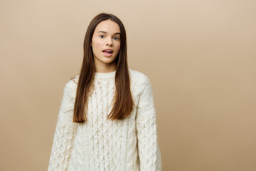 Obraz premium an elegant woman stands on a light background in a white sweater posing standing still and calmly looking at the camera, holding her hands up and lowering them