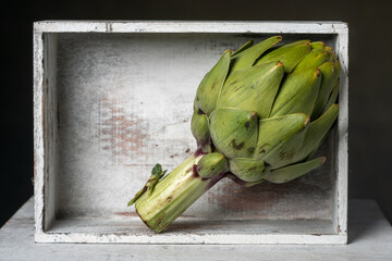 Fresh artichoke on rustic wooden stands, against a dark, moody background. Close-up view, highlighting the texture and natural beauty of the vegetable