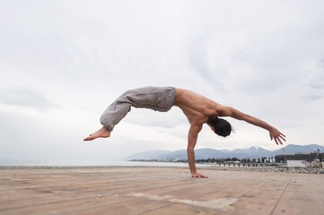 Fototapeta premium Shirtless caucasian man doing backflip on pebble beach. 