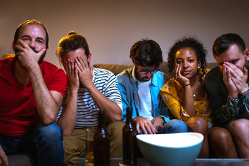Group of friends watching football game on tv worried and sad because their team is losing. Soccer....