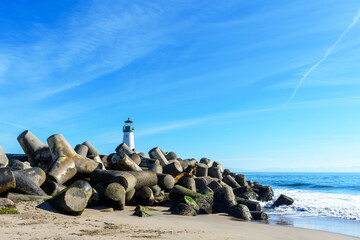 Concrete blocks protecting the jetty of Santa Cruz Harbor. Santa Cruz Breakwater Lighthouse - obrazy, fototapety, plakaty