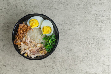 chicken porridge or bubur ayam. Asian or Indonesian style of chicken porridge. topped with shredded chicken, egg, and fried shallot on black bowl