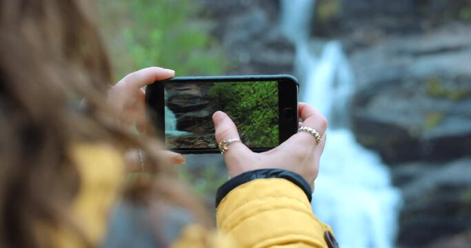 Travel, phone and photography woman at waterfall for backpack adventure, hike and journey memory. Earth, freedom and vacation adventurer girl with smartphone screen for nature pictures.