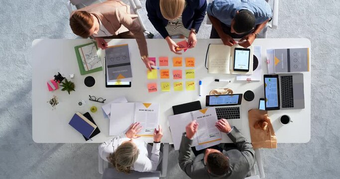 Business people, team and meeting with planning and brainstorming ideas with postit notes, technology and workspace top view. Collaboration, strategy and teamwork, table with project goals and work.