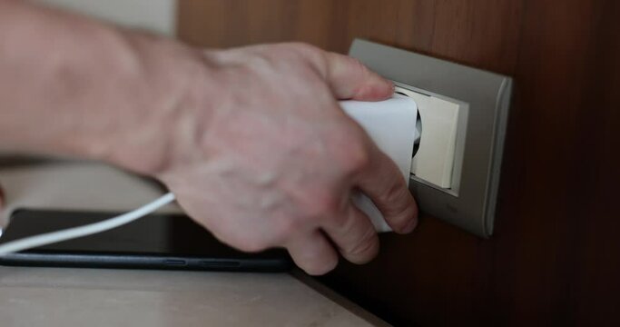 Hand inserts plug into electrical outlet charges phone from usb device