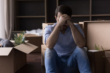 Sad desperate depressed homeowner, renter man leaving out from apartment, sitting at heap of...