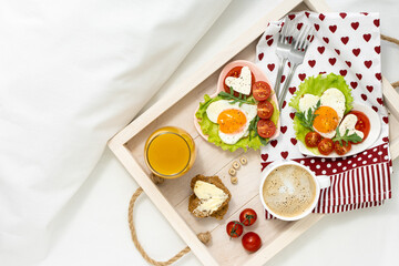 Breakfast in bed on a tray on Valentine's Day. tray with two heart-shaped plates with roasted eggs, tomatoes and cheese, coffee and juice. Breakfast in a hotel room for two persons. View from above.