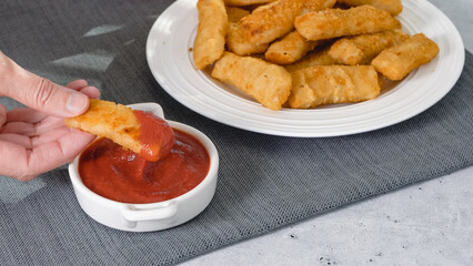 Fish sticks in a crunchy golden breading and bowl of ketchup close-up