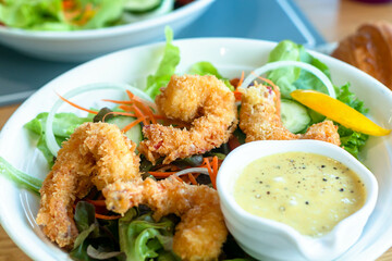 Fried or battered shrimp salad with apple corn carrot tomato with green vegetables and salad dressing on black dish and wooden table for diet food or healthy cuisine 