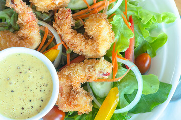 Fried or battered shrimp salad with apple corn carrot tomato with green vegetables and salad dressing on black dish and wooden table for diet food or healthy cuisine 