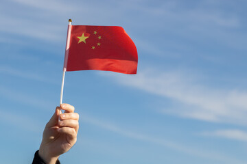Chinese flag in hand flutters in the wind against the sky