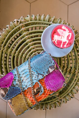 Woman using mobile phone, texting message and drinking coffee. Stylish bag on table. Wearing grey dress and orange plaid. Enjoying cozy morning in cafe with wood interior.