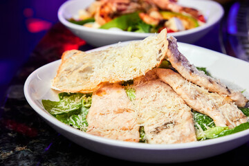 A plate of Caesar salad with chicken breast and parmesan