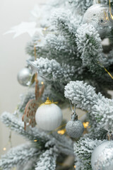 fir tree branches covered with artificial snow, white and silver bulbs, baubles, golden garlands. Christmas tree closeup