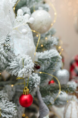 fir tree branches covered with artificial snow, white red and silver bulbs baubles, golden garlands. Christmas tree closeup
