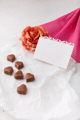 14 February Heart shaped chocolates, fabric rose on white paper, blank postcard. Valentines day sweets and presents