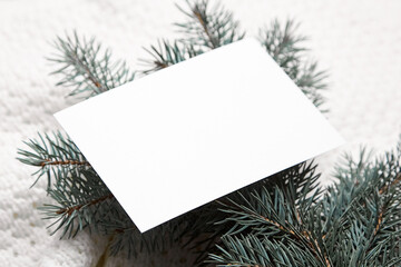 Christmas greeting card mockup with fir tree branches on white knitted pullover background, closeup