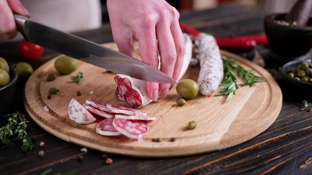 Woman slicing Traditional fuet salami sausage on wooden cutting board at domestic kitchen
