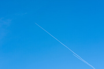 A plane flying high in the sky leaving a white trail on a blue cloudless sky. Travel concept. Bright blue sky gradient background. Cloudless empty sky. Natural background