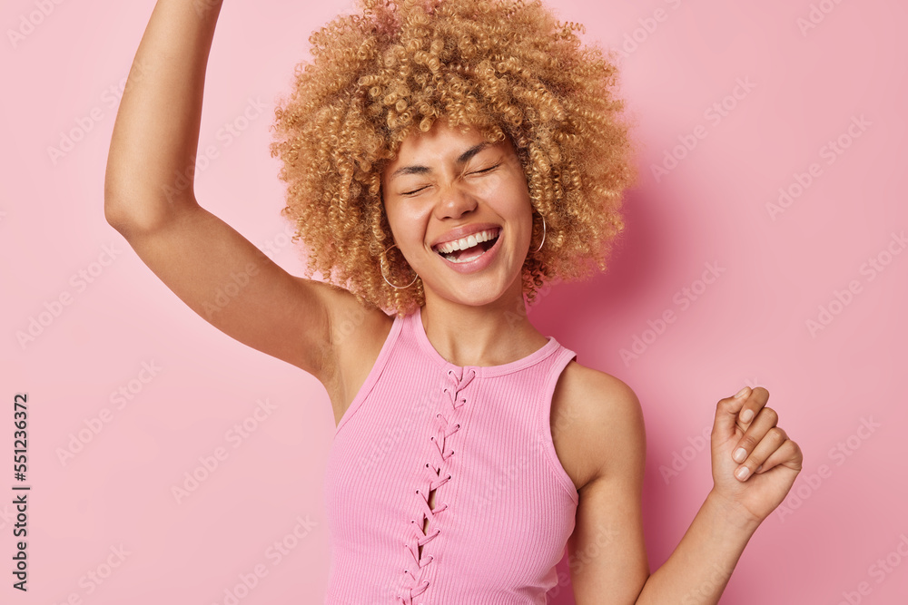 Wall mural joyful woman with curly hair dances carefree keeps arms raised up laughs positively feels like trium - Wall murals