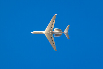 Fototapeta na wymiar White private jet against blue sky traveling west