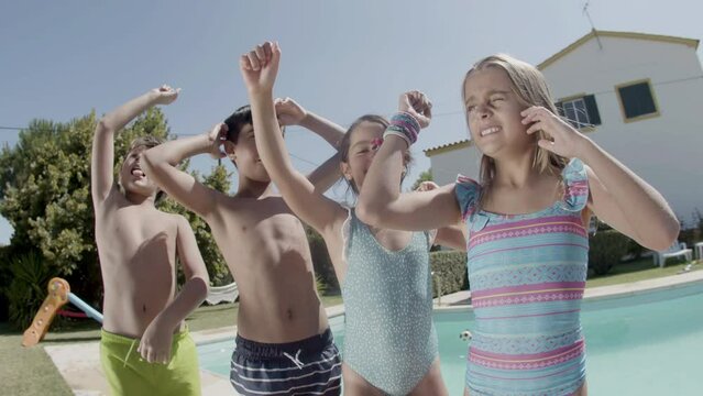 Children dancing at poolside raising hands, having fun together. Boys and girls in swimwear showing excitement, jumping with hands up in the air. Happiness, childhood, summer concept.