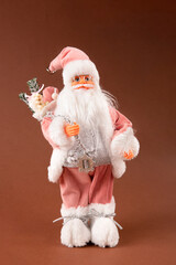 A funny Santa Claus toy with a bag of gifts on its back and a Christmas tree in its hand and pink pants.