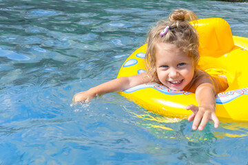 Fototapeta na wymiar Happy white caucasian girl 2 years old with blond hair on an inflatable ring while swimming