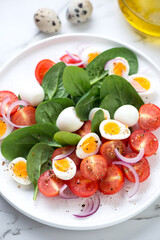 Close-up of salad with spinach leaves, red cherry tomatoes, quail eggs and red onion served on a white plate, vertical shot