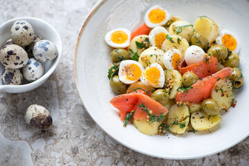 Plate of salad with baby potato, smoked red fish fillet, quail eggs and green olives, selective focus, close-up