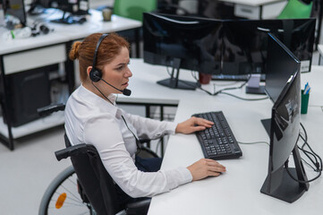 Red-haired caucasian woman in a wheelchair talking on a headset. Female call center worker at her...
