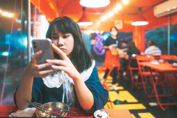 Young adult southeast asian woman using smartphone dinner at Pojangmacha korea style street food...