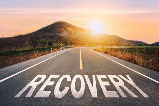  recovery written on highway road in the middle of empty asphalt road of asphalt road at sunset.Road to recovery with sunbream . Challenge with success concept and natural background idea.