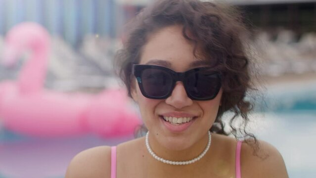 Headshot portrait of happy cheerful curly Caucasian girl student with sunglasses, looks at camera, winks happily smiling. Millennial carefree lady with white toothed smile enjoying summer vacation