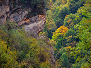 Fototapeta na wymiar Walking path around the mountain covered with green mixed forest. North Ossetia, Alagir Gorge. Dangerous path around the cliff.