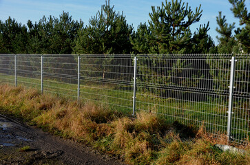 a solid wire fence encloses the garden. the welded wire meshes are strong and can be inserted between the prisms of the bars. the posts are concreted into the concrete slab fence, meadow