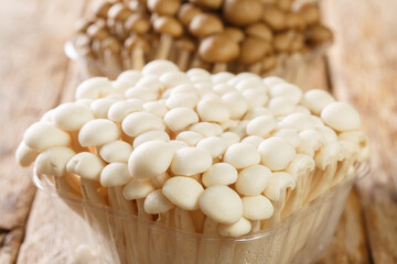 White and brown edible beech mushrooms or Shimeji or buna and bunapi in plastic container closeup on wooden table. Horizontal
