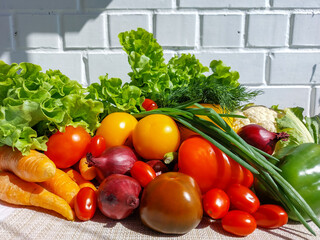 Fresh, healthy and colorful vegetables in bright sunlight with white brick wall in background. Tomatoes, onions, carrots, peppers, cauliflower, salad, dill and champignons