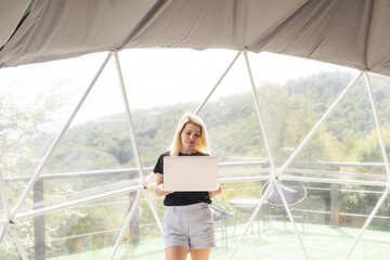 Happy young woman chatting online by using laptop in dome camping. Glamping vacation concept