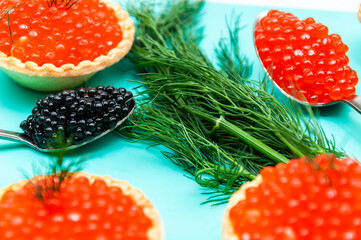 Red and black caviar on a blue tray with cutlery and tartlets.