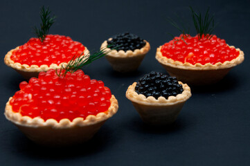 Red and black caviar in tartlets on a black background.